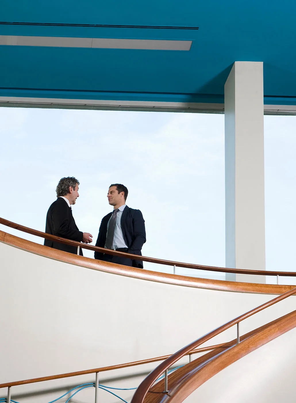 Two businessman hold a conversation on a balcony.